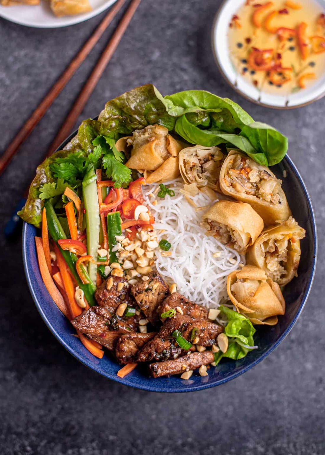 A vermicelli bowl with grilled BBQ pork, spring rolls, fresh herbs and vegetables